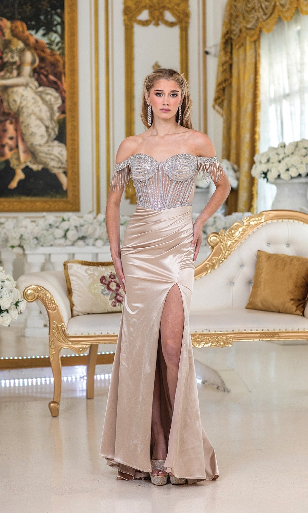 A woman wearing the Dancing Queen 4513, a champagne-colored off-the-shoulder prom dress with a high-leg slit and sheer embellished bodice, stands in an ornate gold and white room.